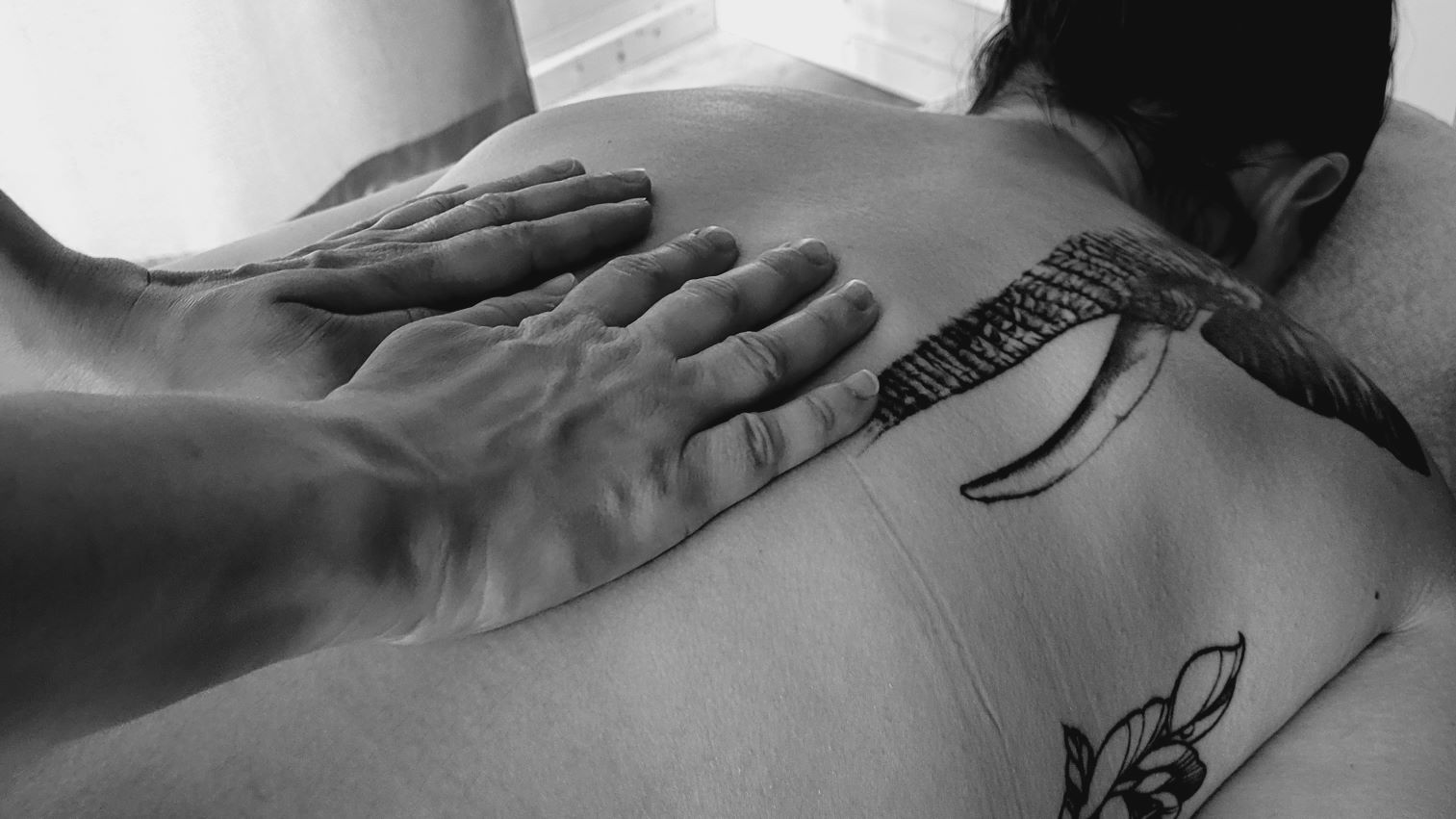 Photo de la doula r'Eve posant les mains sur le dos d'une femme qui a un tatouage d'éléphant