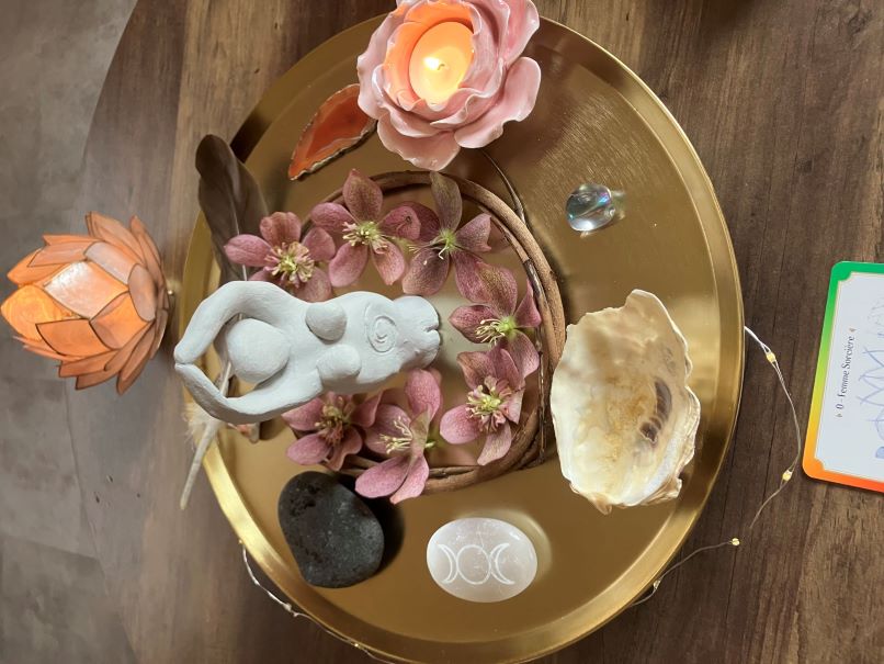 Photo d'un plateau avec une statuette représentant une femme, des fleurs, des pierres et des bougies posé sur un autel lors d'un cercle de femmes proposé par la doula r'Eve