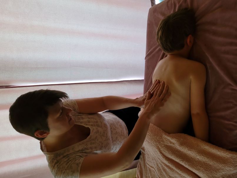 Photo de la doula r'Eve massant le dos d'un enfant allongé sur la table de massage