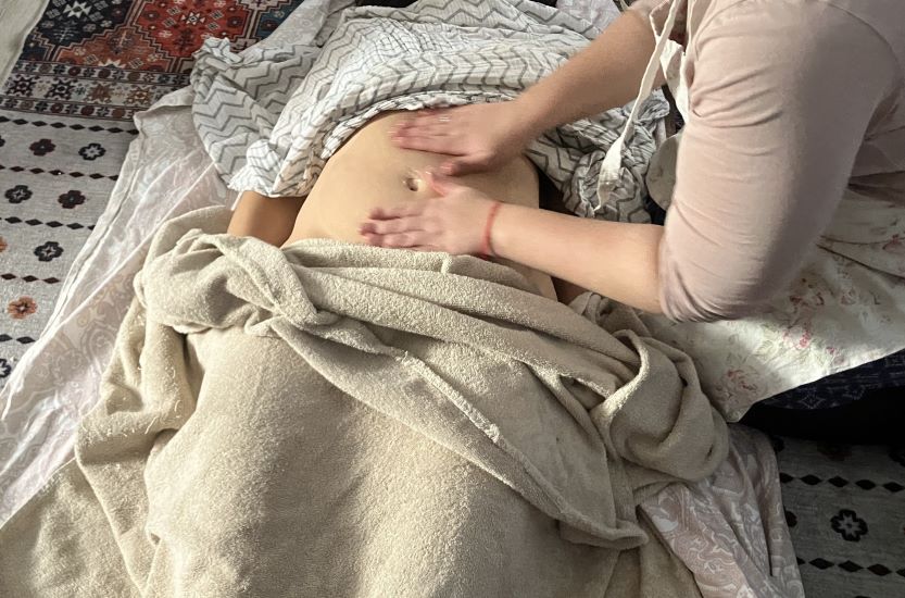 Photo d'une femme posant les mains sur le ventre d'une autre femme enveloppée dans des rebozos lors d'un soin des matrones